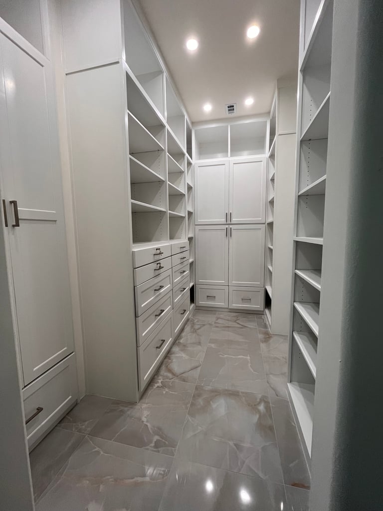 Modern white walk-in closet with built-in shelving, storage drawers, and polished marble flooring