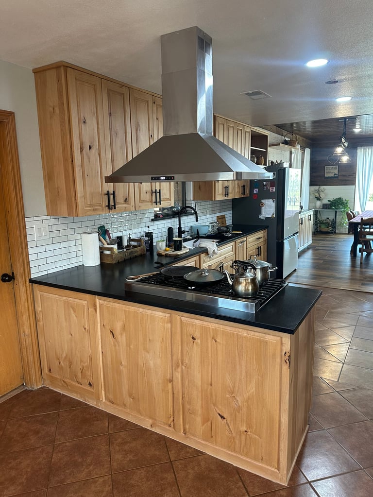 Modern kitchen with wooden cabinets, black granite island countertop, stainless steel range hood, and white subway tile backsplash