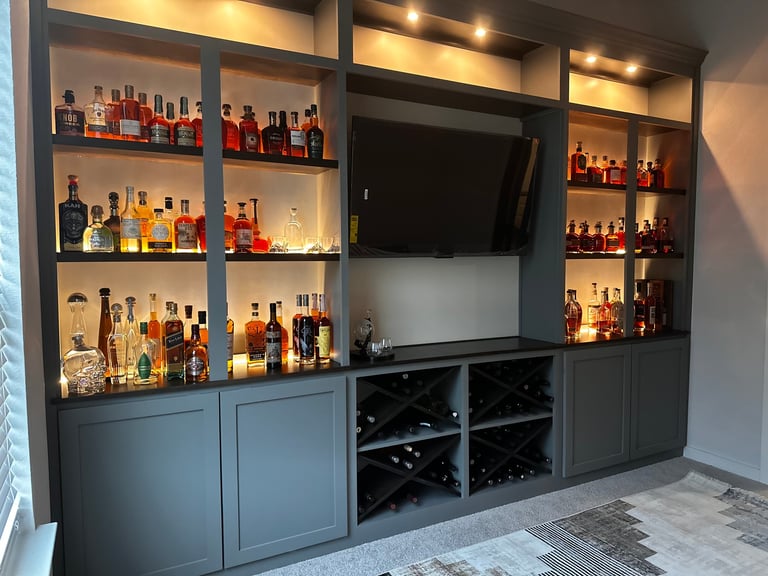 Modern home bar entertainment unit with illuminated shelves displaying liquor bottles, flat-screen TV, and wine storage