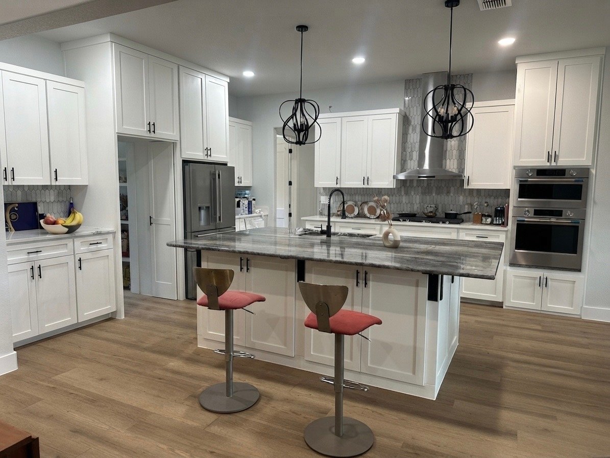 Modern kitchen with white cabinetry, stainless steel appliances, island with red bar stools, marble countertops, and wooden flooring