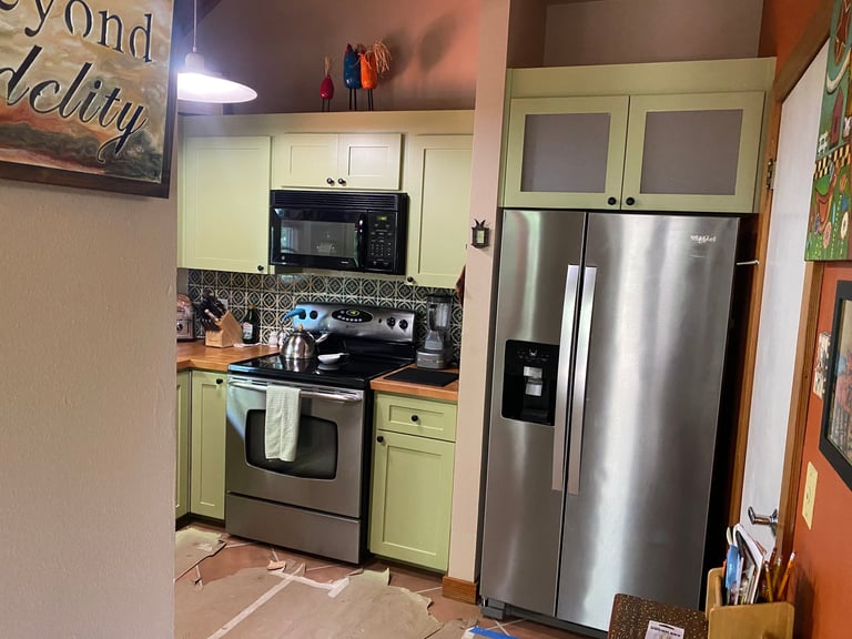 Small kitchen with pale green cabinets, stainless steel appliances, black stovetop, and tiled backsplash in a compact space