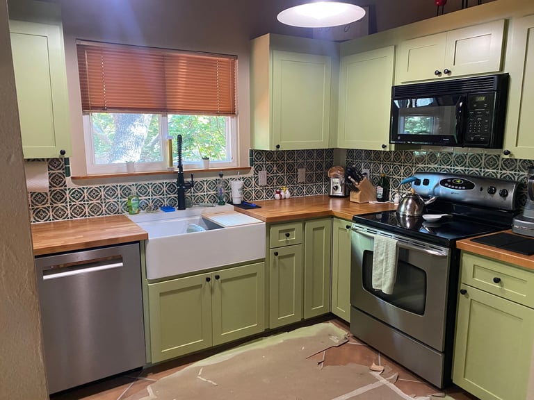 Modern kitchen with sage green cabinets, stainless steel appliances, patterned tile backsplash, and wooden countertops