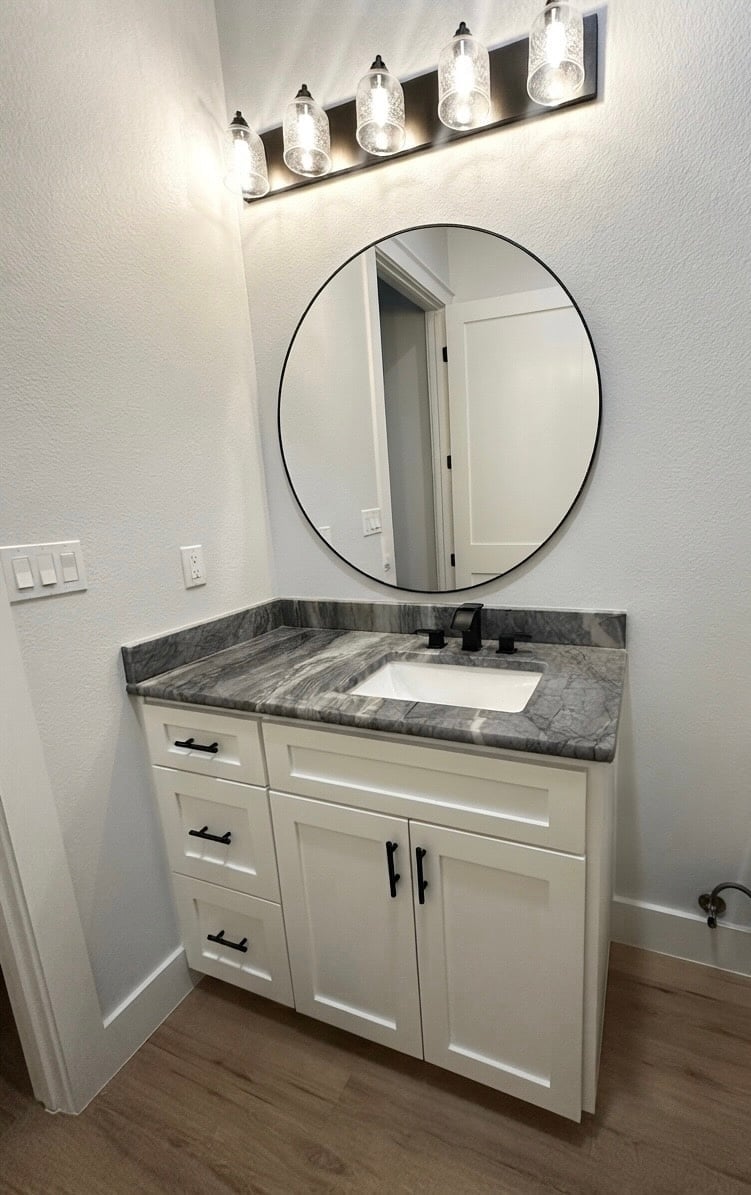 Modern bathroom vanity with white cabinetry, marble countertop, and round mirror
